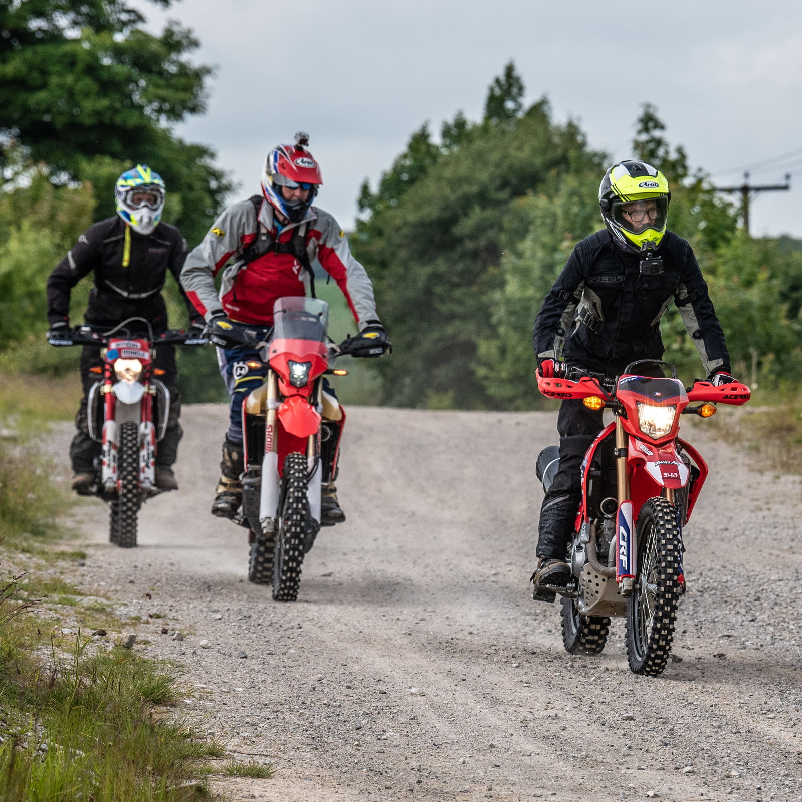 Three motorbikes riding along a green lane
