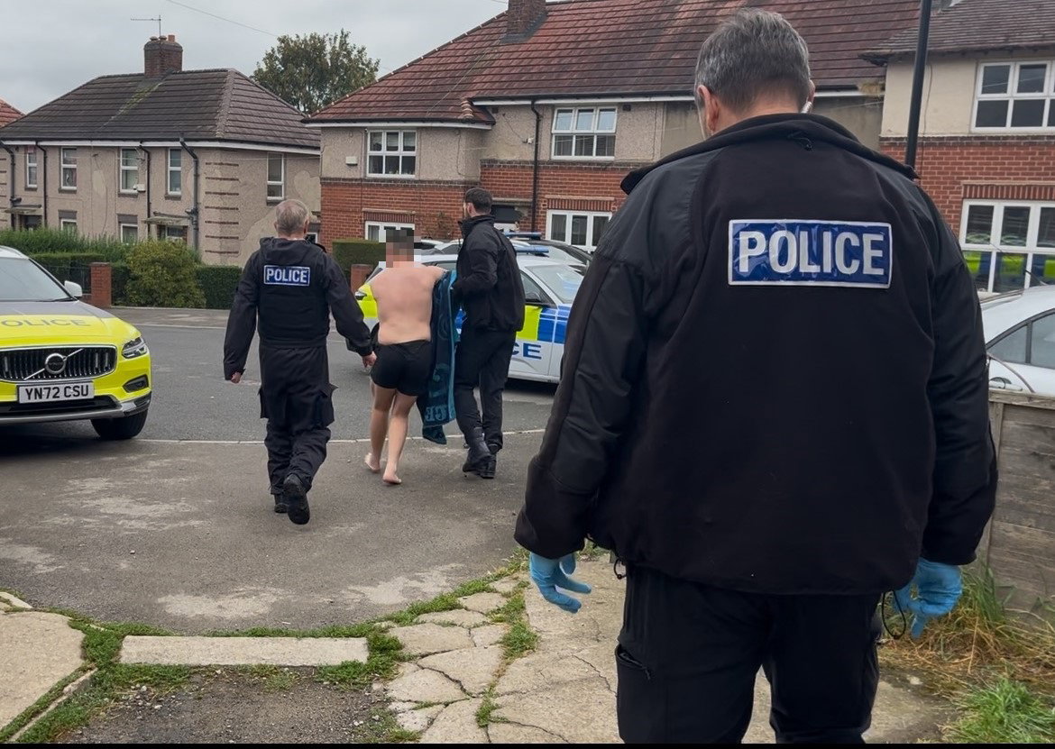 one suspect being walked to a police car following the raid