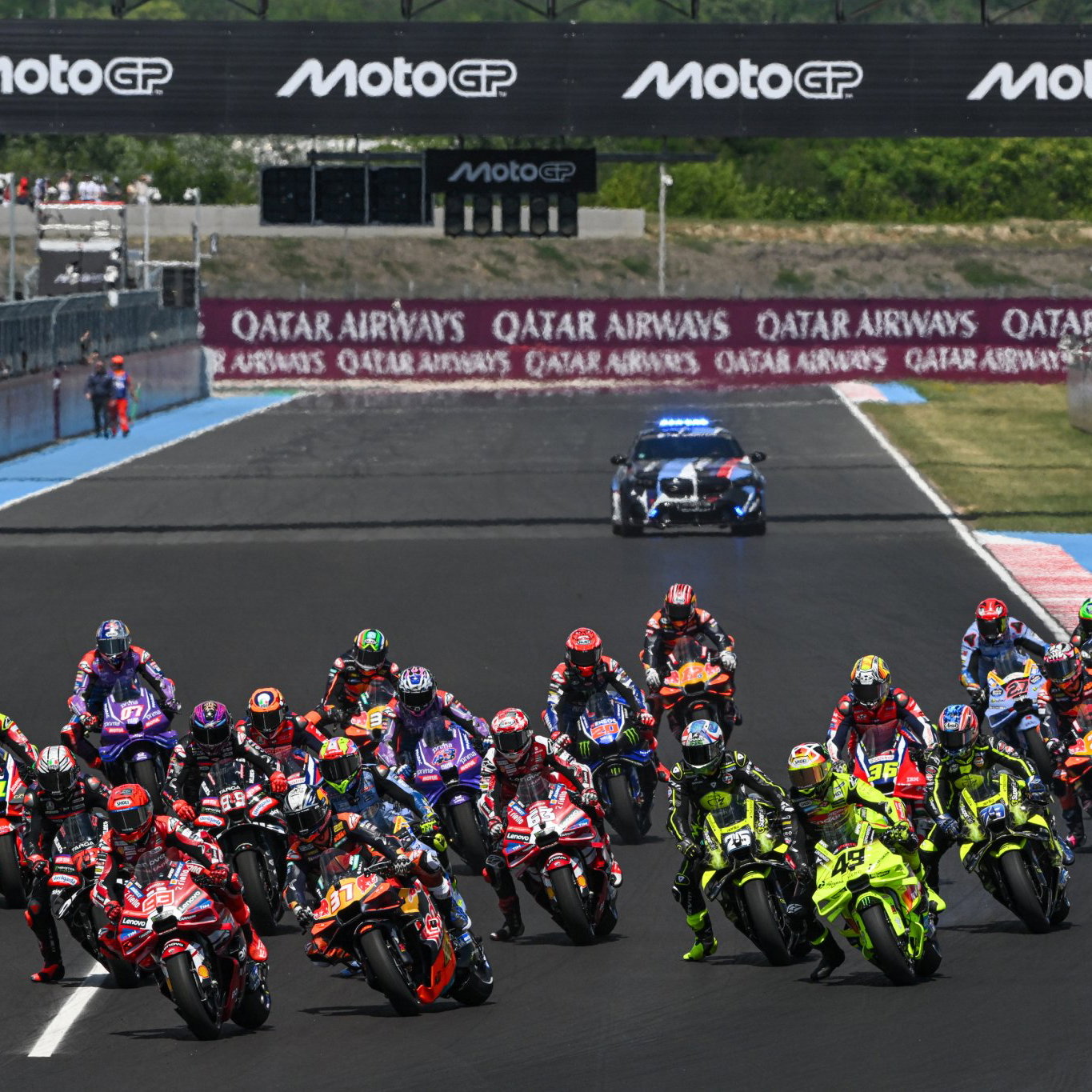A grid of MotoGP bikes heading into a turn