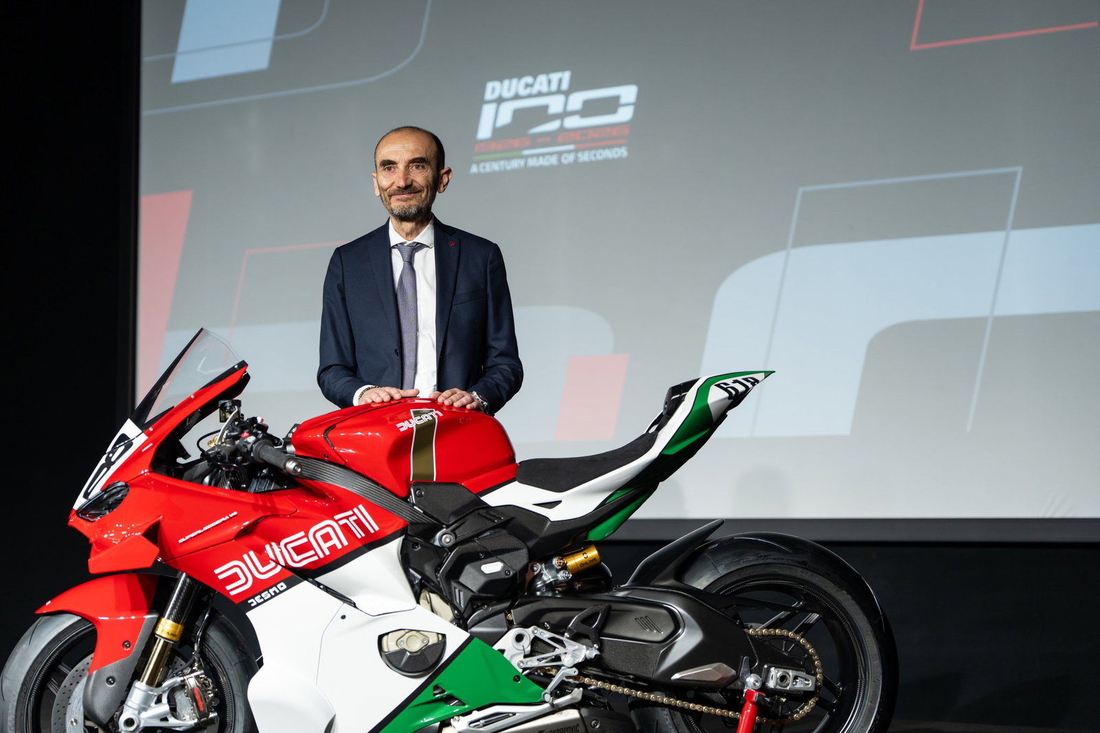 Claudio Domenicali standing with a Ducati motorcycle.