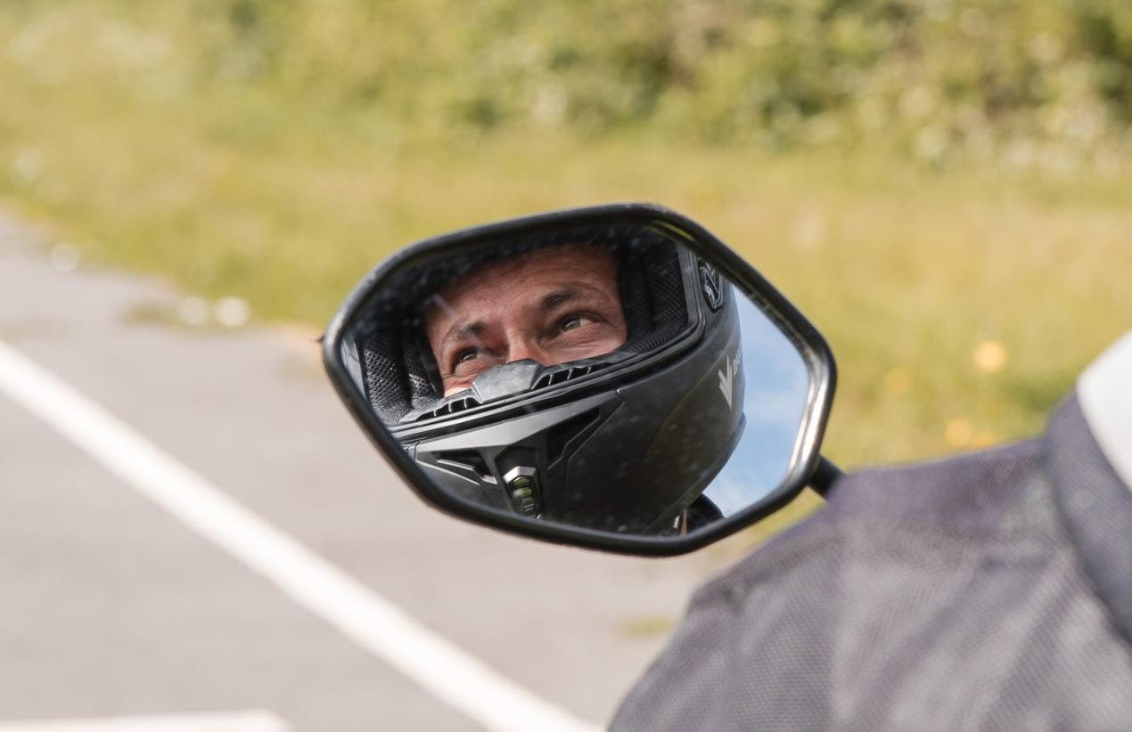 A rider's face reflected in a rear-view mirror