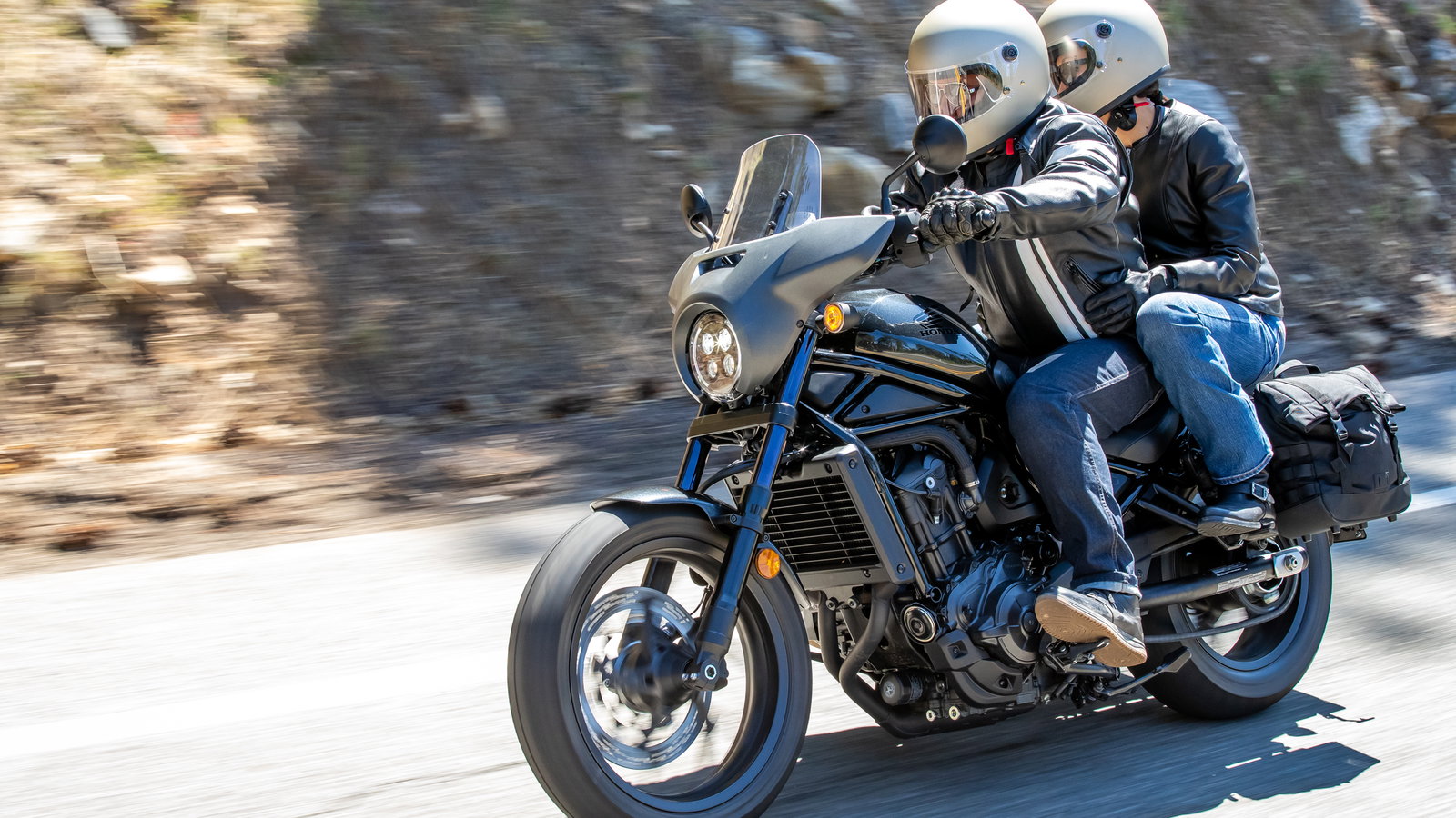 A cruiser motorcycle with a rider and pillion on a sunny day